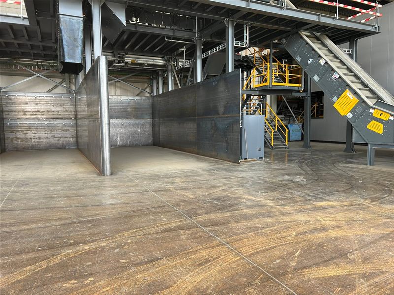 Stalen bunkerwanden in een industriële hal, met een geel bordes en trappen op de achtergrond